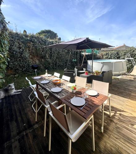 une table en bois avec des chaises et un parasol sur une terrasse dans l'établissement La Family House - Calme & Spacieuse, 20mn Plages & Montpellier, à Vendargues