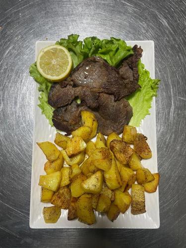 a plate of food with meat and potatoes and a lemon at GRAND JNK Boutique Hotel in Kukës
