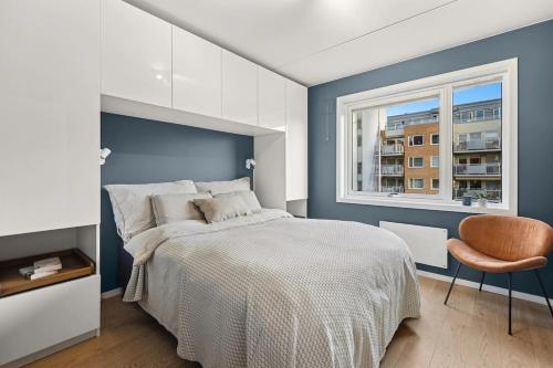 Un dormitorio con una cama y una ventana y una silla. en Modern 3 bedroom apartment - 4 minute walk from metro - top floor baclony view, en Oslo