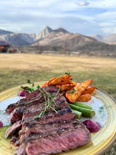 a plate of meat and vegetables with mountains in the background at Pensiunea Bodrogeni in Poiana Aiudului