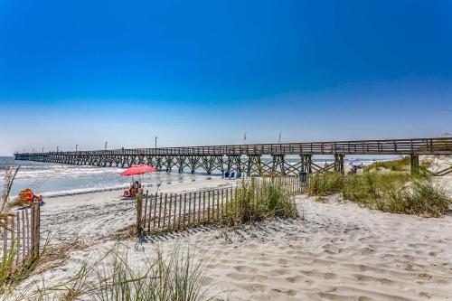 a beach with a pier and a red umbrella at Drifty Daze Oceanfront Suite w Pool in Myrtle Beach