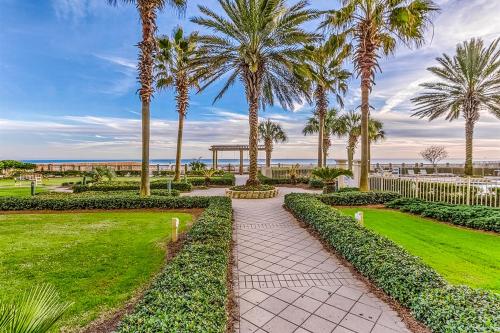 a walkway through a park with palm trees and the ocean at The Beach Club 609A in Gulf Highlands
