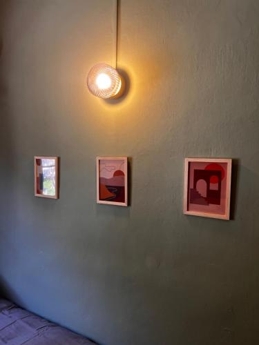three framed paintings on a wall with a light at Hôtel Fleur des Alpes in La Brigue