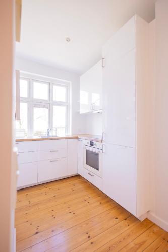 a kitchen with white cabinets and a wooden floor at Central Lyngby Apartments in Kongens Lyngby