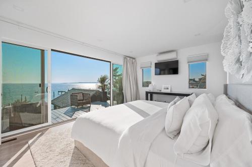 a white bedroom with a large bed and a balcony at Private beach on a fenced in property sunset views in Hampton Bays