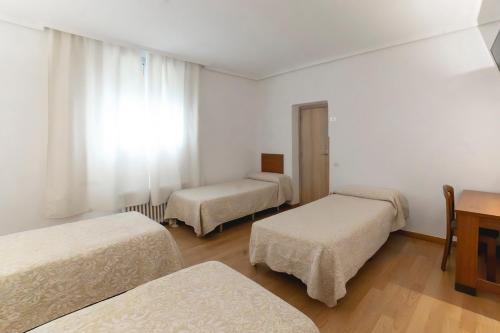 a room with three beds and a desk at Hotel Pedro Torres in Cuenca