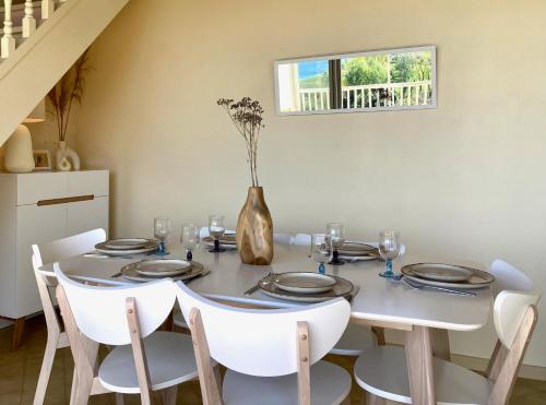ein Esstisch mit weißen Stühlen und einer Vase mit Blumen in der Unterkunft Appartement Les marines du soleil in Patrimonio