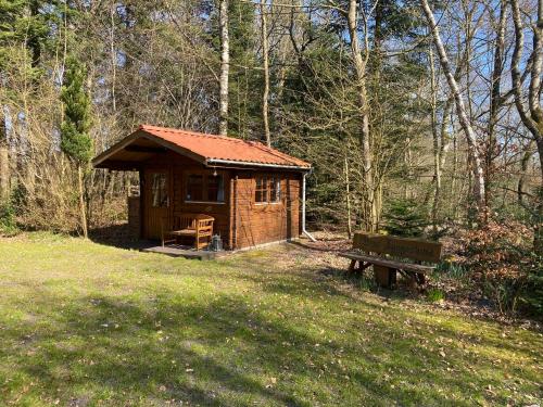 a small wooden cabin in the woods with a bench at Krogager Primitiv Camping - Krogen in Grindsted