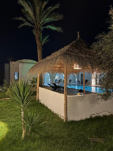 a villa with a straw umbrella and a swimming pool at night at Villa des deux oliviers Djerba in Djerba