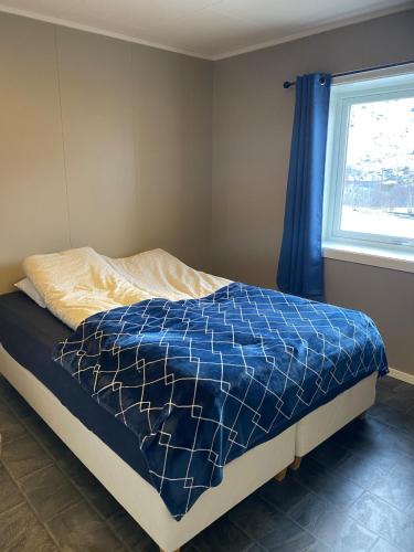 a bed with a blue comforter and a window at House in Vågan in Hopen