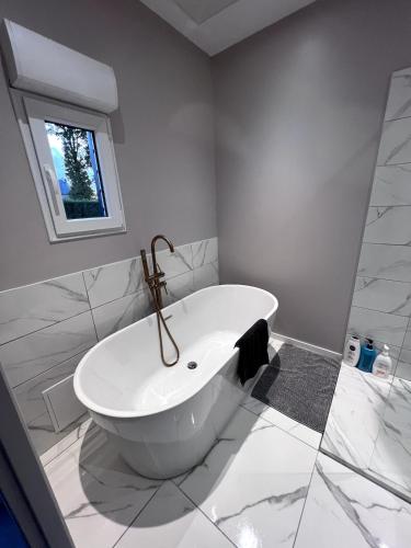 La salle de bains blanche est pourvue d'une baignoire et d'une fenêtre. dans l'établissement Cottage Dolce vita à Bobital, à Bobital