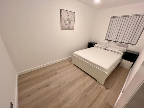 a small bedroom with a white bed and wooden floors at The Premier Living Experience Entire 2-Bedroom Modern Apartment in Bromley