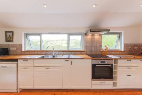 a kitchen with white cabinets and a sink and two windows at Riverside barn on private wildlife estate in Washaway