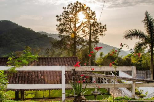 a white fence and a tree with red flowers at Pousada Aconchego Shangrilla in Penedo