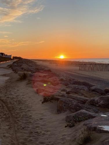 a sunset on a beach with rocks and a fence at La Descenderie - Bord de mer in Sangatte