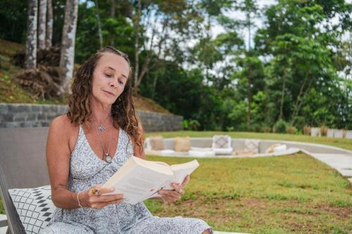 a woman sitting on a bench reading a book at Pandanus Lodge & Retreats Bungalow Orchidee in San Ramón