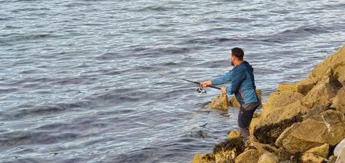 a man standing on some rocks fishing in the water at Over the Fjord in Leikanger