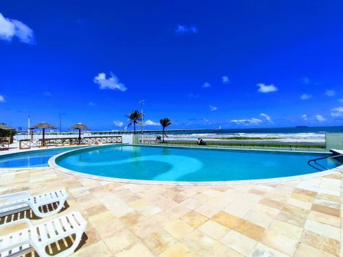 a pool with chairs and the beach in the background at Apartamento a Beira mar de Maceió in Maceió