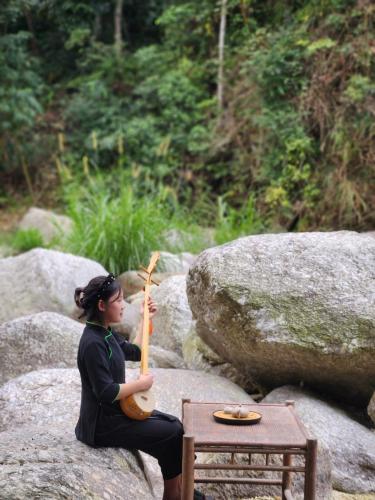 a woman sitting on a rock playing an instrument at Dong Que Homestay-Tours-Motorbike, Car rental, Hiking in Ha Giang
