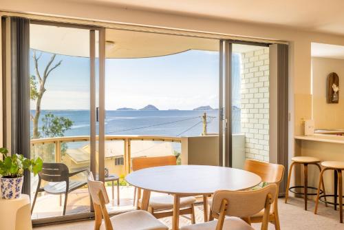 a living room with a table and chairs and a view of the ocean at The Point 13, 5-7 Mitchell St - stunning water views, complex pool and WiFi in Soldiers Point