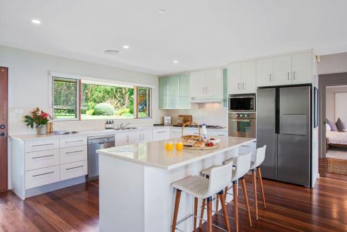 a kitchen with white cabinets and a large island with bar stools at Myava - By Berry Getaways in Berry