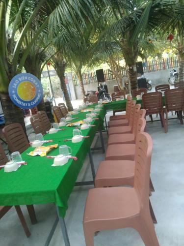 a row of green tables with chairs and palm trees at Homestay sao biển in Phương Phi