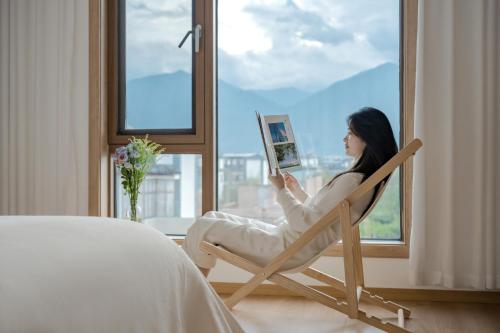 a woman sitting in a chair reading a book at 墨弦苑智能轻奢民宿 喜洲镇海舌公园店 in Dali
