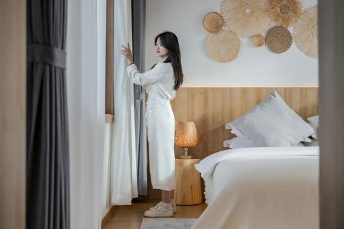 a woman standing in a hotel room looking out the window at 墨弦苑智能轻奢民宿 喜洲镇海舌公园店 in Dali
