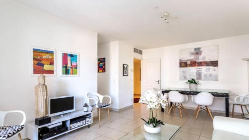 Il comprend un salon doté de murs blancs, d'une télévision et de chaises. dans l'établissement B014 Spacieux 2 chambres piscine parking 4min plage, à Cannes