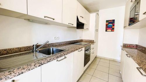 une cuisine avec des armoires blanches et un évier dans l'établissement B014 Spacieux 2 chambres piscine parking 4min plage, à Cannes