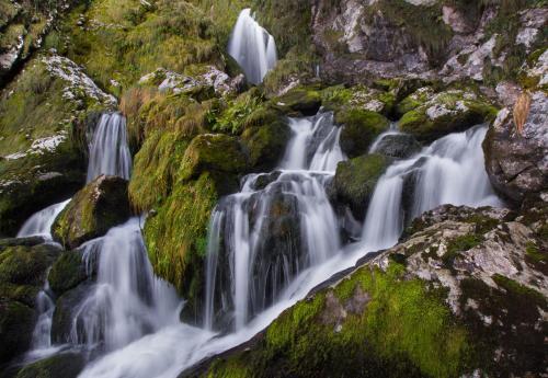 a waterfall on the side of a mountain with mossy rocks at Apartamentos la Regoria in Arenas de Cabrales