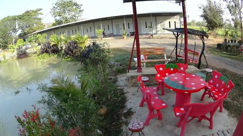 a patio with red tables and chairs next to a pond at เช็คอินรีสอร์ทชัยนาท Check-in resort in Ban Khao Khayai (1)