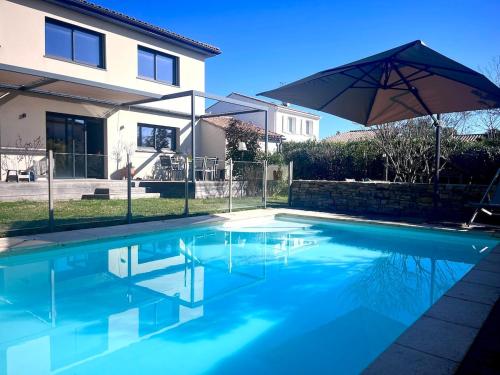 une piscine avec un parasol devant une maison dans l'établissement Belle villa familiale avec piscine, à Teyran