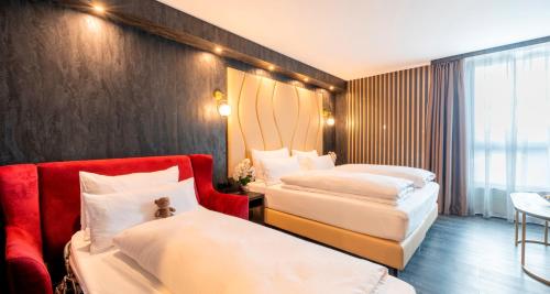 a hotel room with two beds and a red chair at PLAZA Premium Parkhotel Neu-Ulm in Ulm