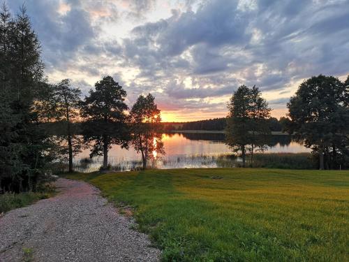 a gravel path next to a lake with the sunset at Ranczo Wyszowate Domki in Wyszowate