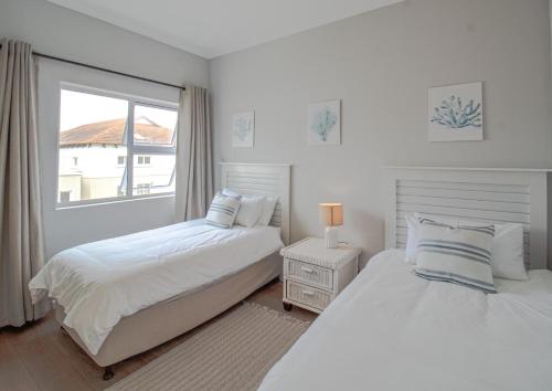 Un dormitorio blanco con dos camas y una ventana. en Seaside Escape at The Dunes: Walk to Beach Braai, en Plettenberg Bay
