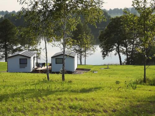 two houses in a field next to a lake at Ranczo Wyszowate Domki in Wyszowate