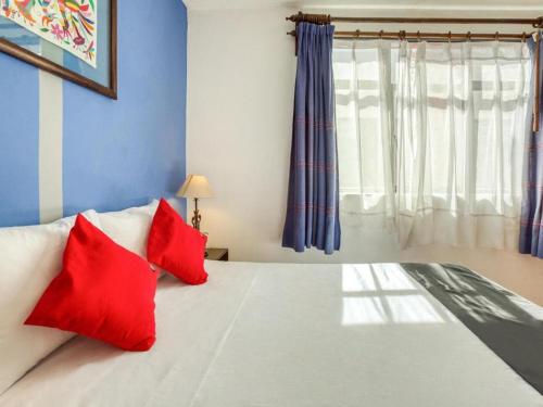 a bedroom with a bed with two red pillows at Capital O Parador Crespo Hotel, Oaxaca in Oaxaca City