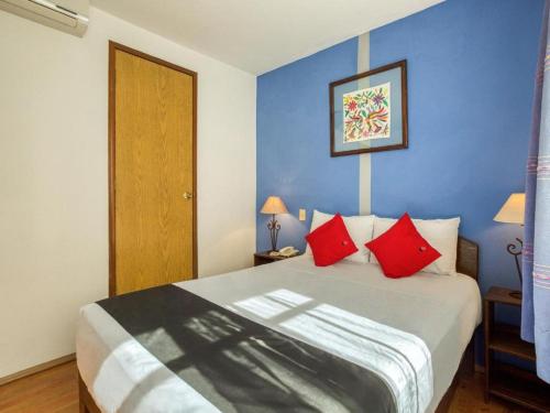 a bedroom with a bed with red pillows and a blue wall at Capital O Parador Crespo Hotel, Oaxaca in Oaxaca City