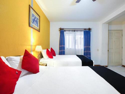 a hotel room with two beds with red pillows at Capital O Parador Crespo Hotel, Oaxaca in Oaxaca City