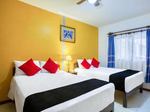 two beds in a room with yellow walls and red pillows at Capital O Parador Crespo Hotel, Oaxaca in Oaxaca City