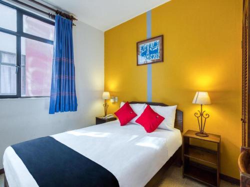a bedroom with a bed with red pillows and a window at Capital O Parador Crespo Hotel, Oaxaca in Oaxaca City