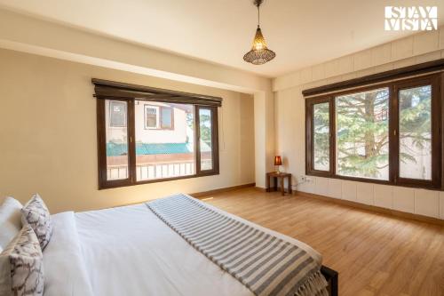 a bedroom with a white bed and two windows at StayVista at The Apricot with Heater & BBQ in Mashobra