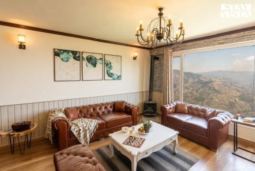 a living room with leather furniture and a large window at StayVista at The Apricot with Heater & BBQ in Mashobra