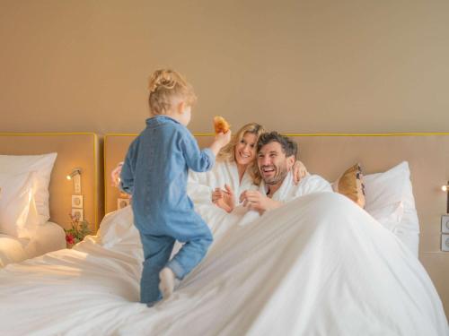 a young child jumping on a bed with a man and woman at Pullman Toulouse in Blagnac