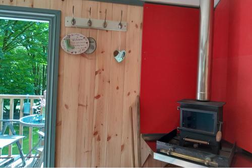 a woodburning stove in a room with a red wall at Little Greenwood Shepherd Hut in Boughton Malherbe
