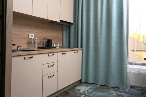 a kitchen with white cabinets and a green curtain at Scandi Hotel in Uralsk