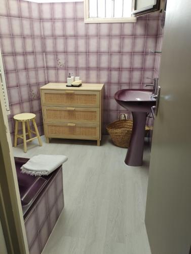 La salle de bains est pourvue de murs carrelés roses, d'un lavabo et d'un tabouret. dans l'établissement Comme chez mamies, à Saint-Dizier