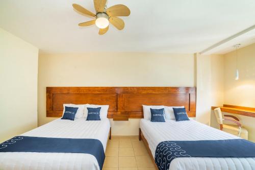 two beds in a hotel room with a ceiling fan at Capital O Hotel Casa Blanca in Celaya