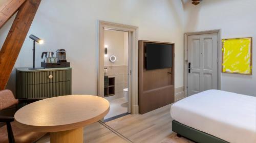a bedroom with a bed and a table and a tv at The College Hotel Amsterdam, Autograph Collection in Amsterdam